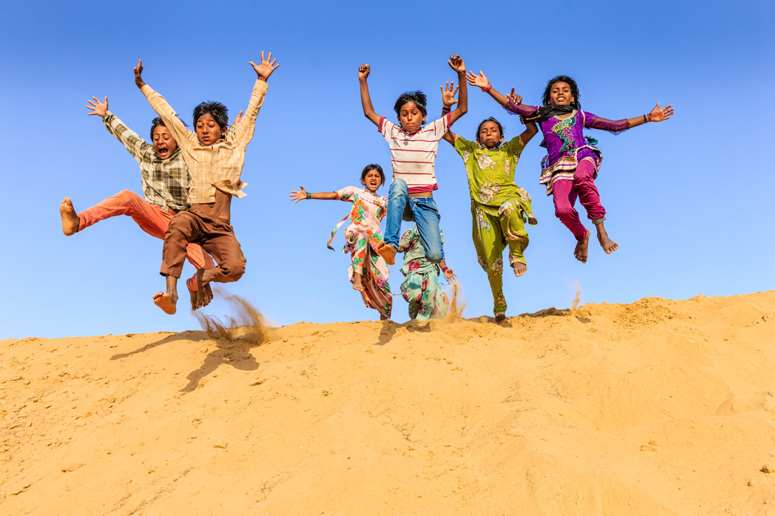 Group of happy Indian children jumping off dune into sand